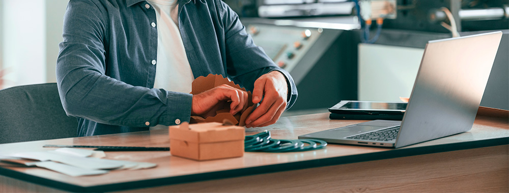 Ambiance atelier prototypage, mains qui testent un emballage avec un produit réel