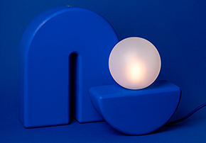 lampe design minimaliste Switch & Match avec base et arche bleues, ampoule posée en équilibre, fond bleu uni
